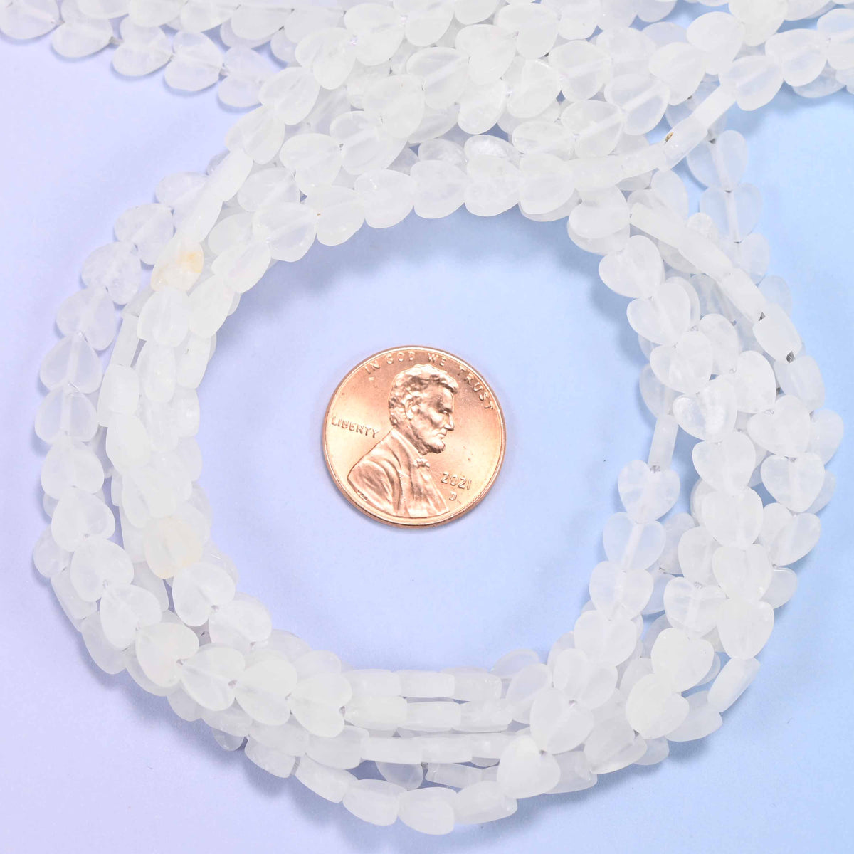 Matte Clear Quartz flat heart bead strands coiled around a US penny for size reference