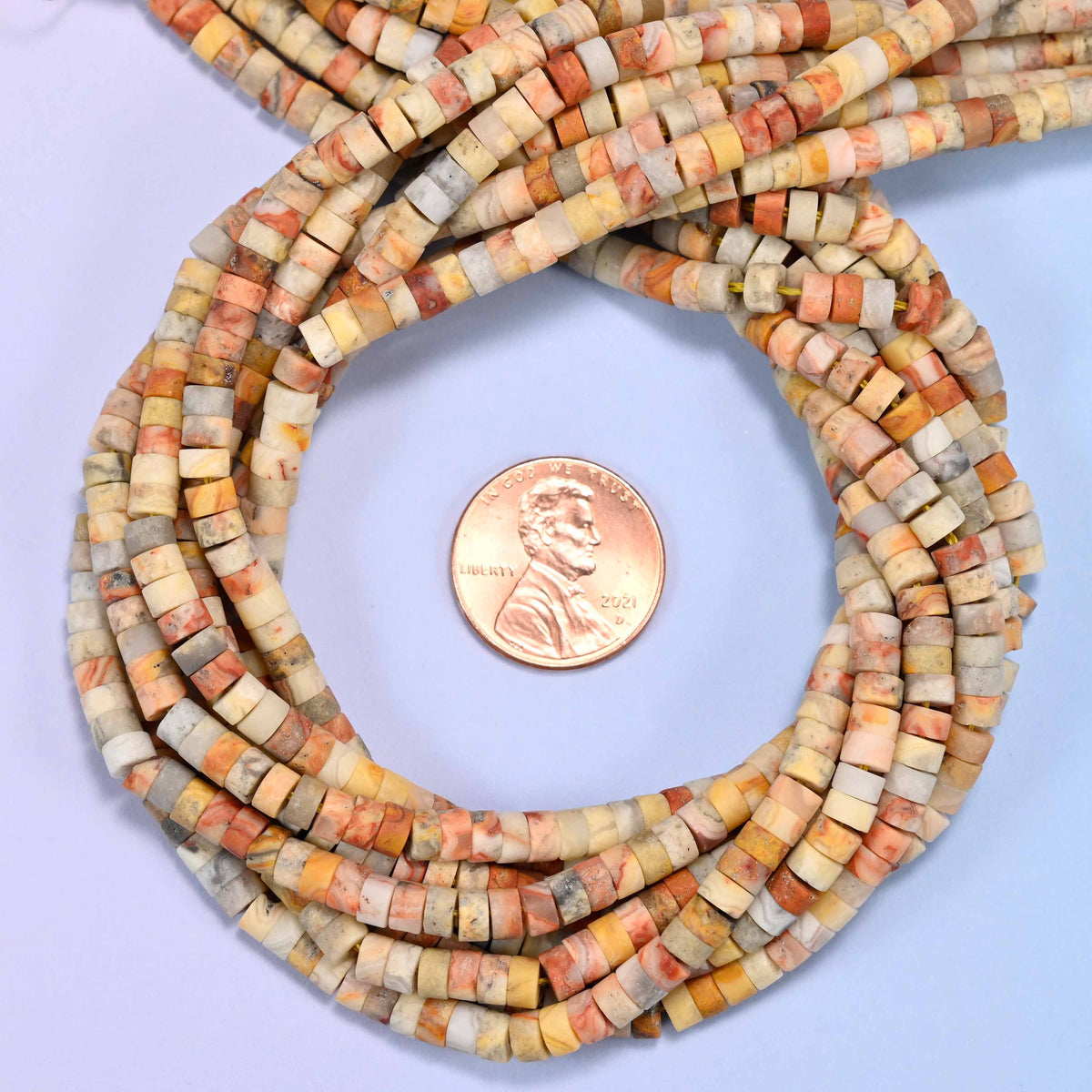 Matte Crazy Agate heishi disc bead strands coiled around a US penny for size reference