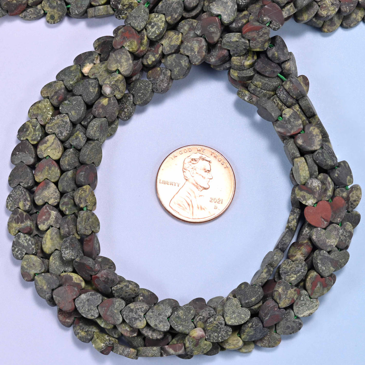 Matte Dragon Bloodstone flat heart bead strands coiled around a US penny for size reference