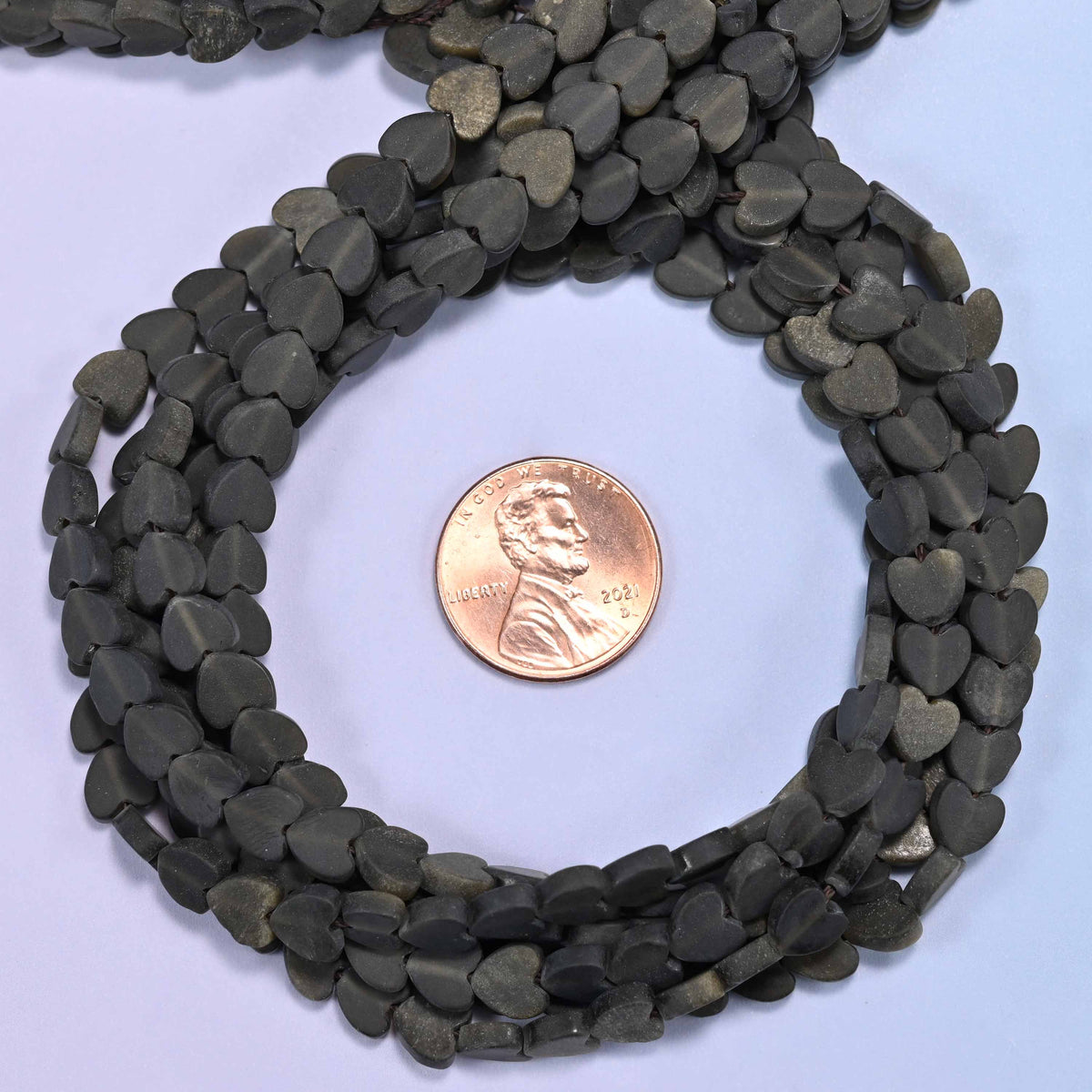 Matte Gold Obsidian flat heart bead strands coiled around a US penny for size reference