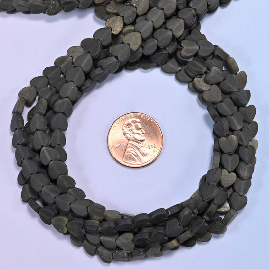 Matte Gold Obsidian flat heart bead strands coiled around a US penny for size reference
