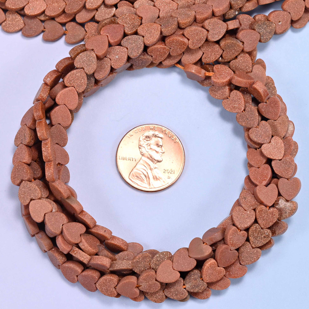 Matte Gold Sandstone flat heart bead strands coiled around a US penny for size reference