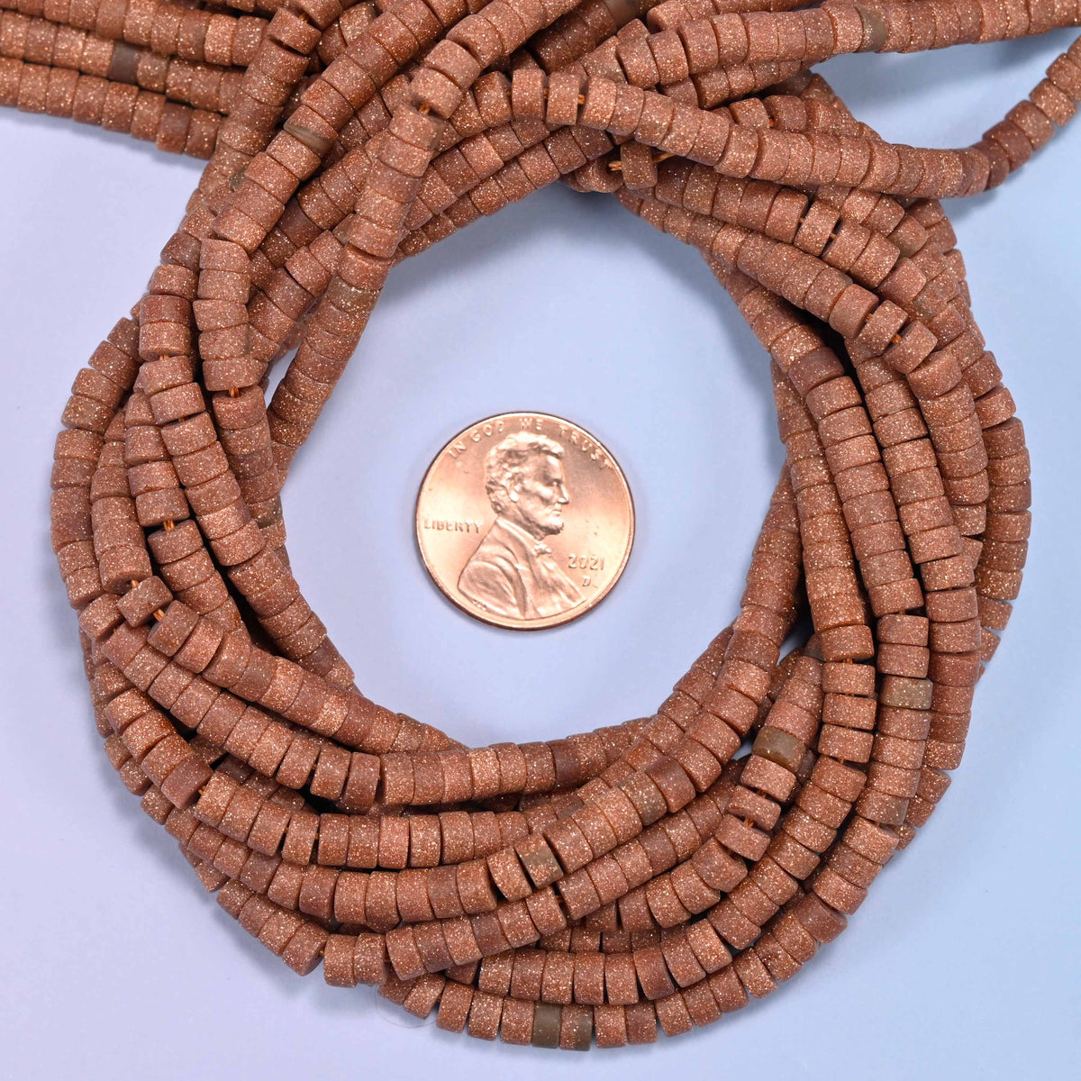 Matte Gold Sandstone heishi disc bead strands coiled around a US penny for size reference