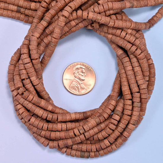 Matte Gold Sandstone heishi disc bead strands coiled around a US penny for size reference