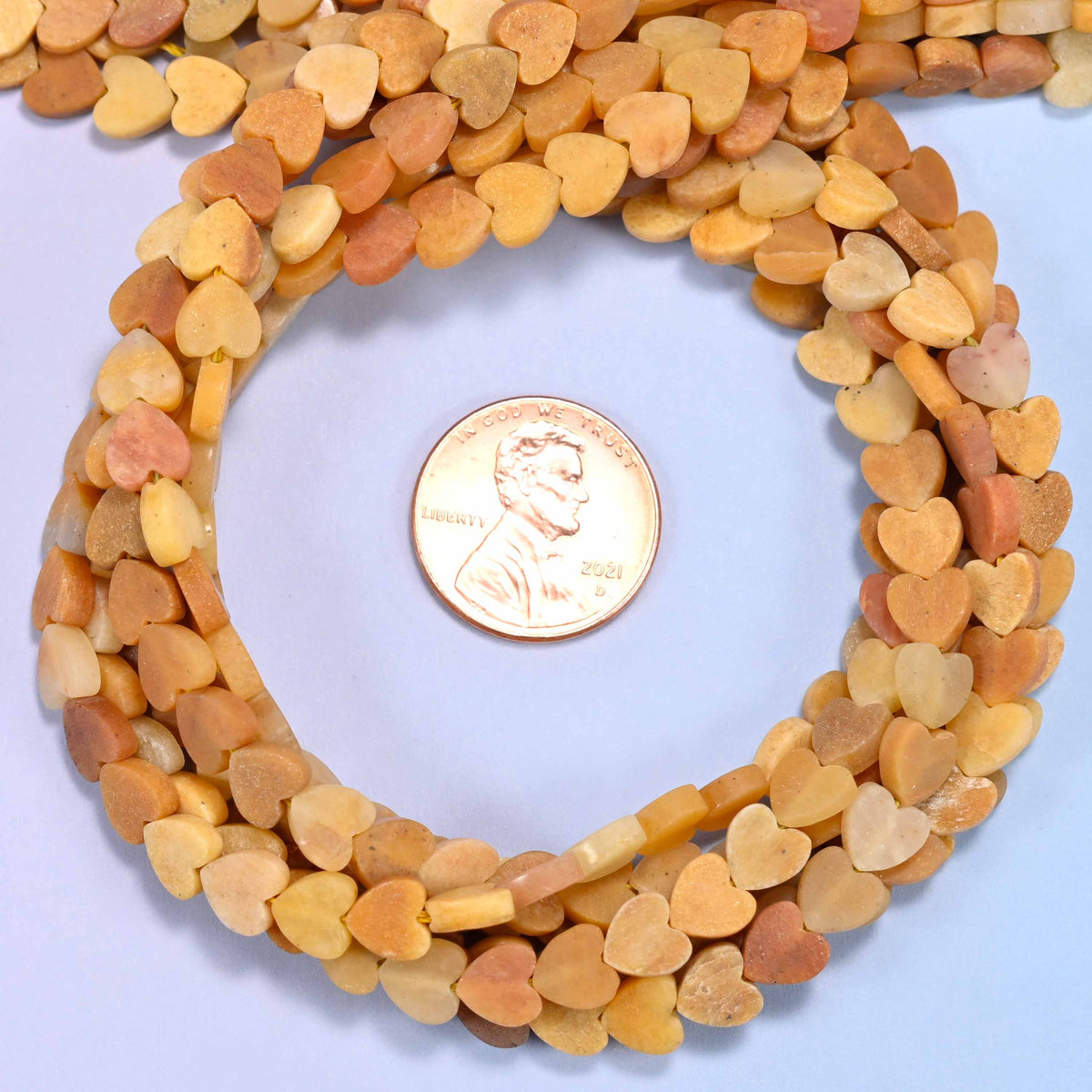 Matte Gold Silk Jade flat heart bead strands coiled around a US penny for size reference