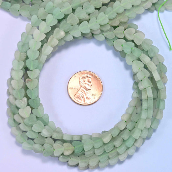 Matte Green Aventurine flat heart bead strands coiled around a US penny for size reference