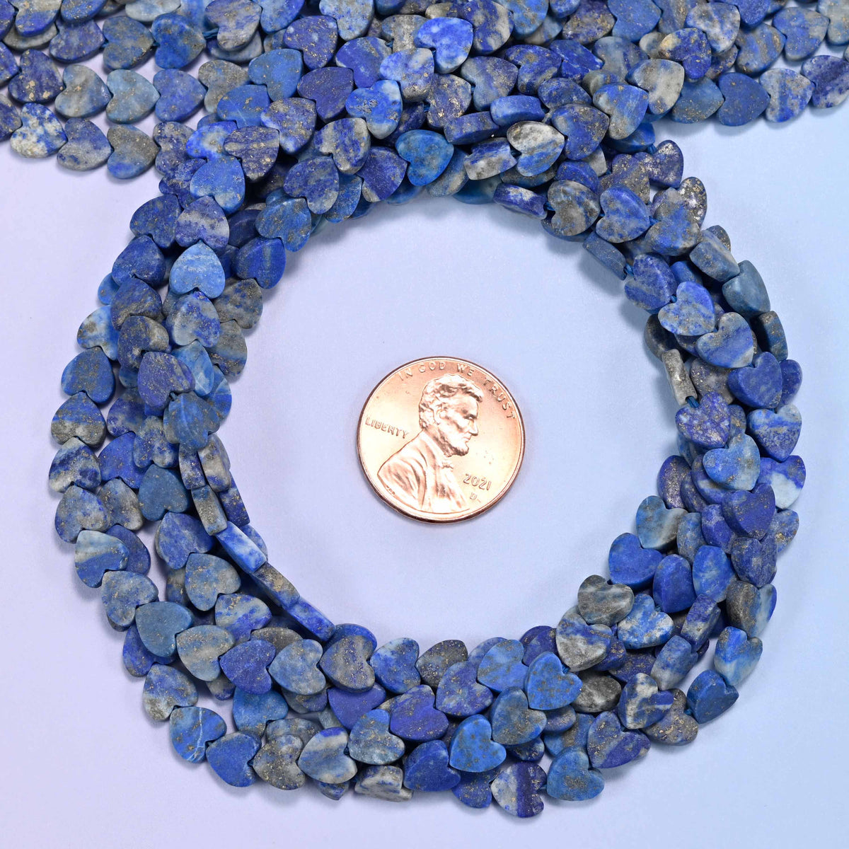 Matte Lapis Lazuli flat heart bead strands coiled around a US penny for size reference