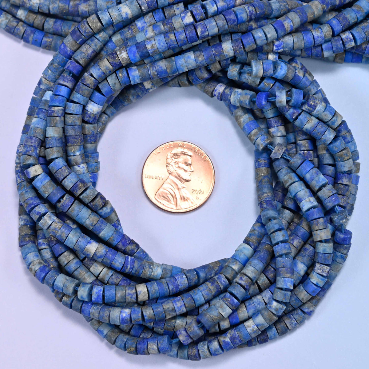 Matte Lapis Lazuli heishi disc bead strands coiled around a US penny for size reference