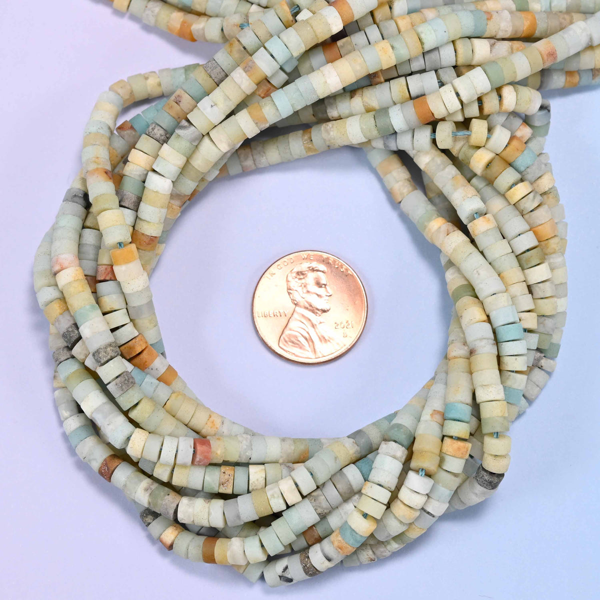 Matte Multicolor Amazonite heishi disc bead strands coiled around a US penny for size reference