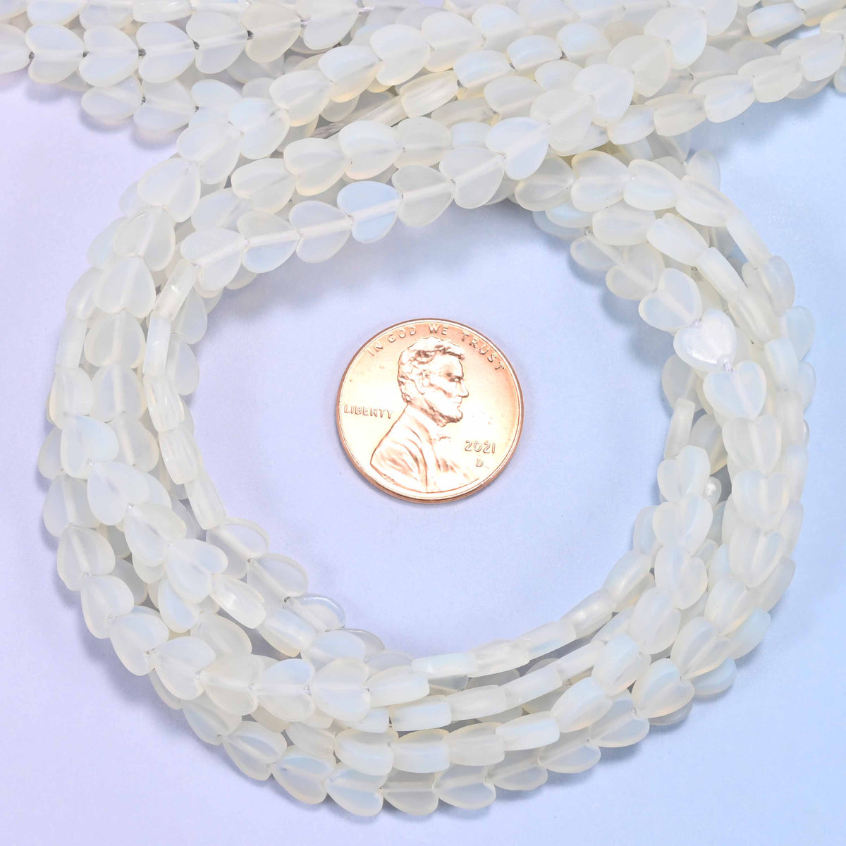 Matte Opalite flat heart bead strands coiled around a US penny for size reference