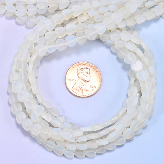 Matte Opalite flat heart bead strands coiled around a US penny for size reference