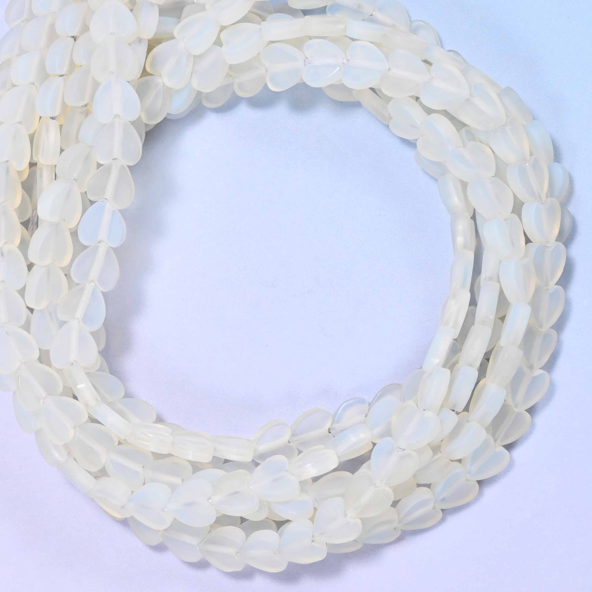 Matte Opalite flat heart beads, close view of the coiled strands of milky white hearts with a matte finish