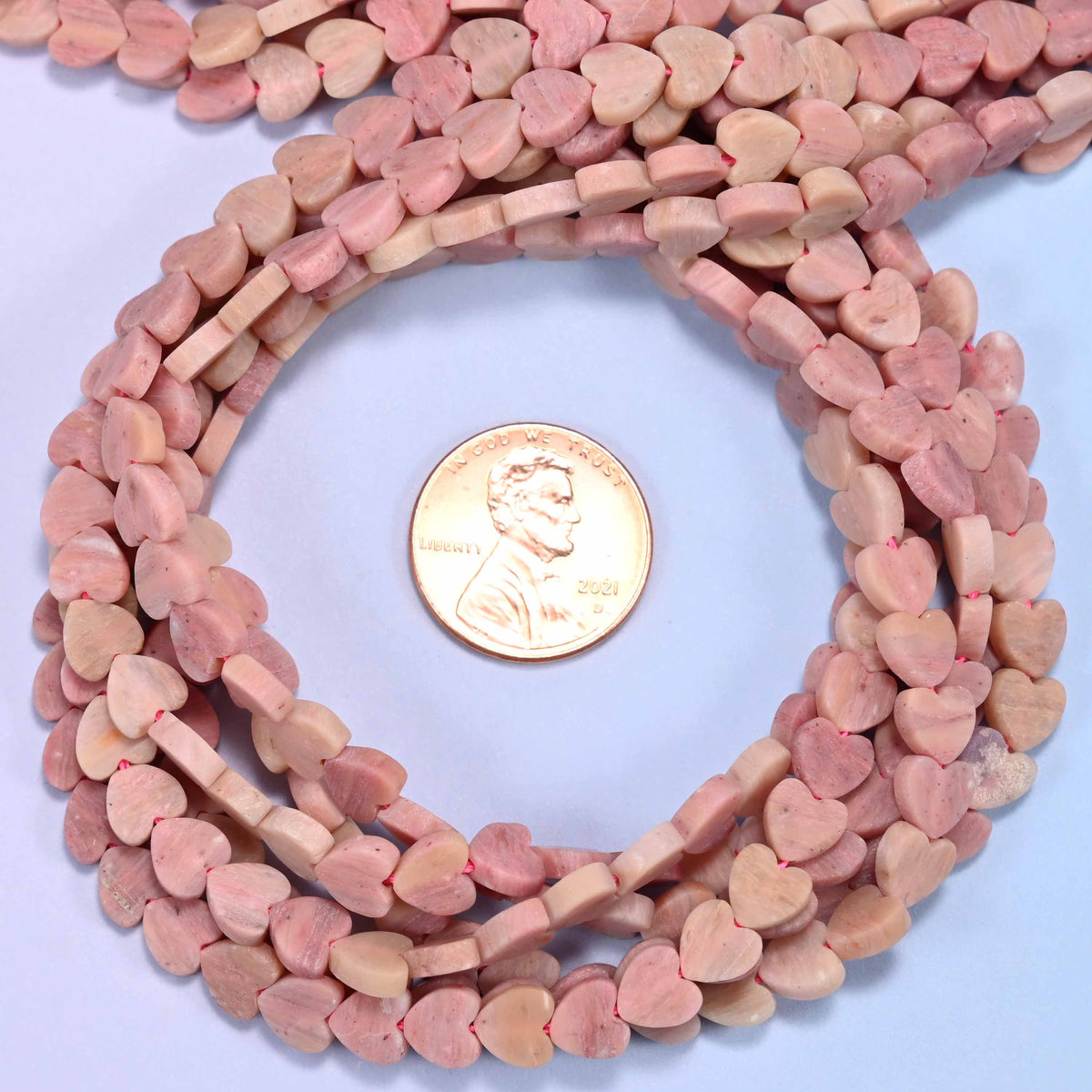 Matte Pink Rhodonite flat heart bead strands coiled around a US penny for size reference