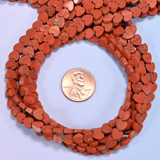 Matte Red Jasper flat heart bead strands coiled around a US penny for size reference