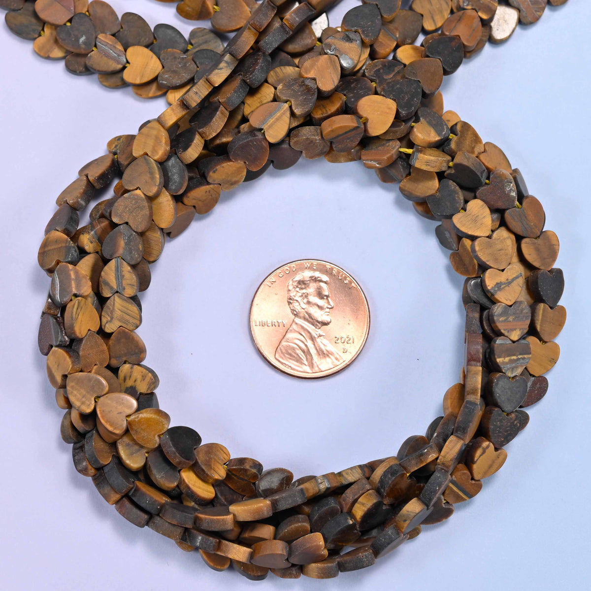 Matte Tiger Eye flat heart bead strands coiled around a US penny for size reference
