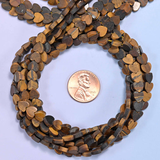 Matte Tiger Eye flat heart bead strands coiled around a US penny for size reference