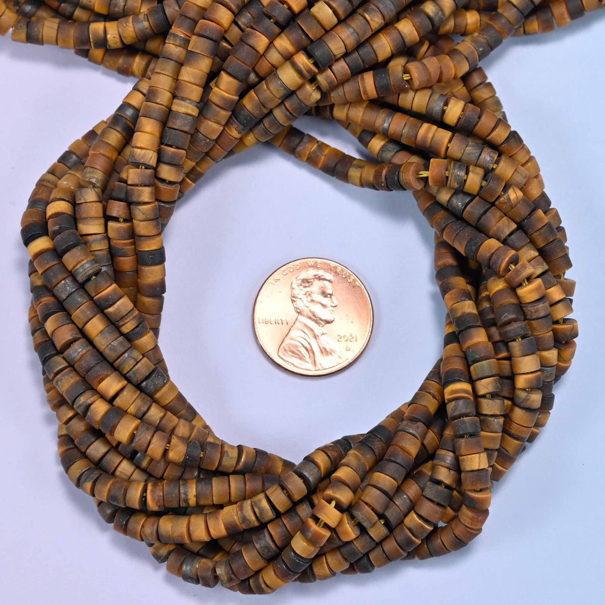 Matte Tiger Eye heishi disc bead strands coiled around a US penny for size reference