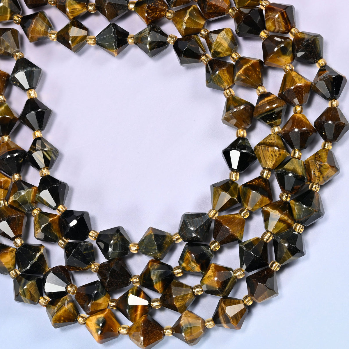 10mm Iron Tiger Eye faceted bicone beads coiled into a loose circle on a light lavender background.
