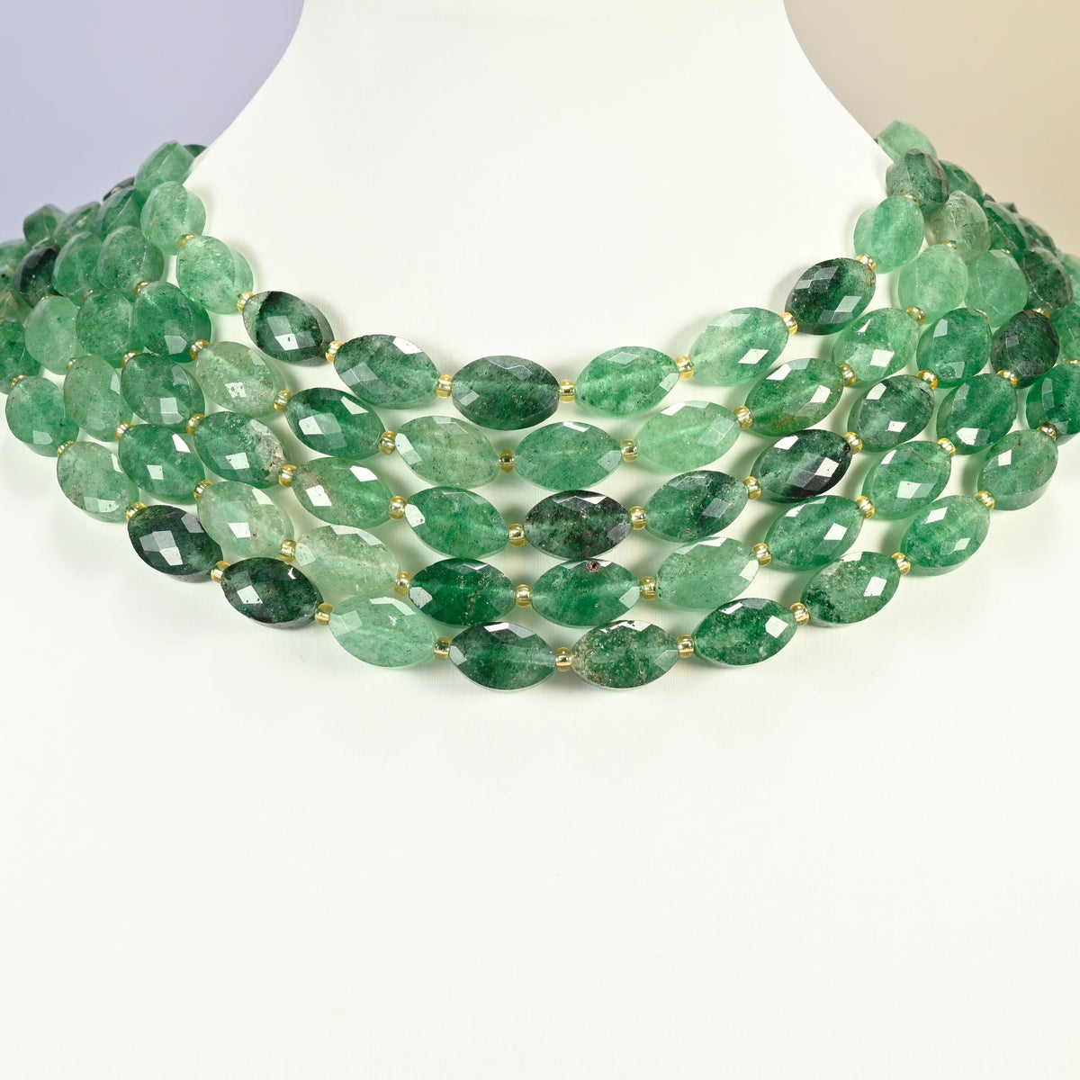 Green strawberry quartz faceted flat oval strands arranged as a layered collar on a white display bust, deep green beads across the neck