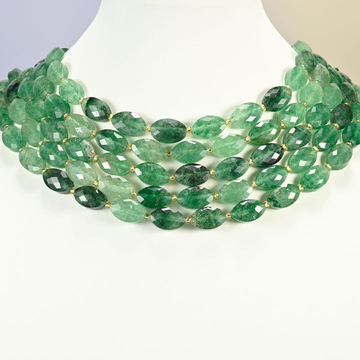 Green strawberry quartz faceted flat oval strands arranged as a layered collar on a white display bust, deep green beads across the neck