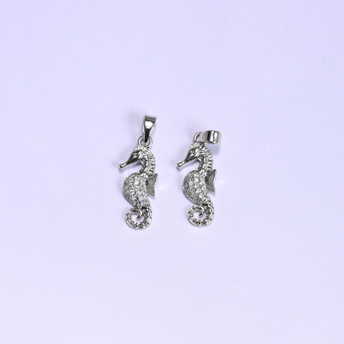 Sea horse zirconia pendants in platinum silver tone, a pair of 18K plated charms shown front-on and turned to show the bail, clear zirconia pave across the body and curled tail.