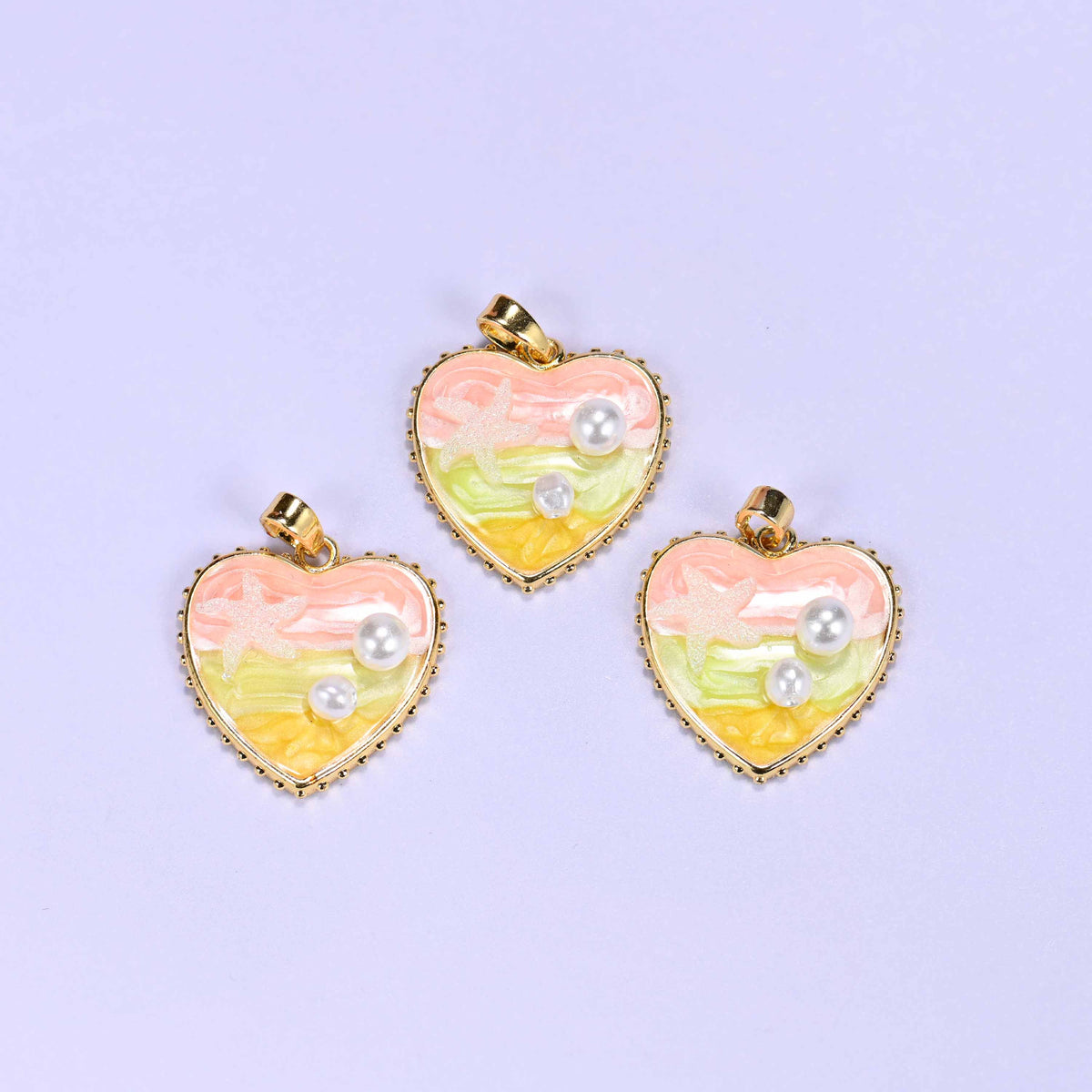 Enamel Heart Pendants in pink, a trio of gold-plated hearts with pink-to-yellow swirled enamel and faux pearl detailing.