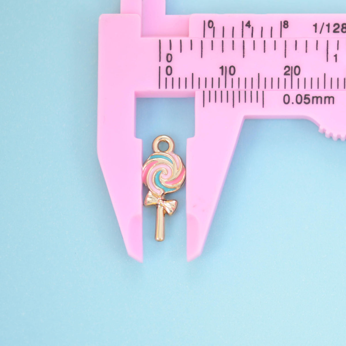 Enamel lollipop charm measured lengthways in a pink caliper, about 16mm including the stick.