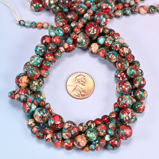 Red sea sediment jasper round beads coiled in loose rings with the knotted strand end at the top, shown with a US penny for scale.
