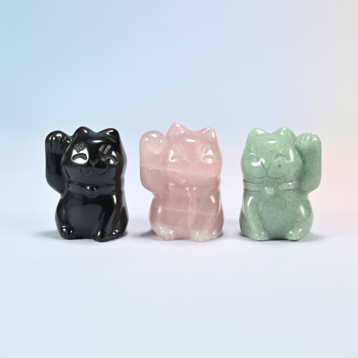 Three 1.8 inch waving cat crystal carvings in natural black obsidian, rose quartz and green aventurine, each with a raised paw