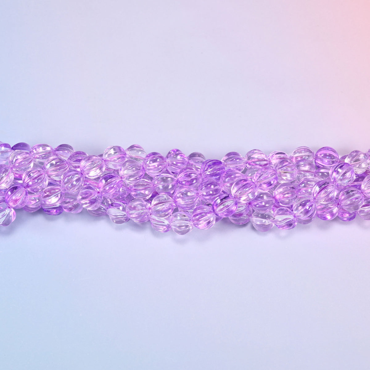 Clear purple pumpkin glass beads, 8mm melon rounds, strands laid in a gentle wave straight across the frame.
