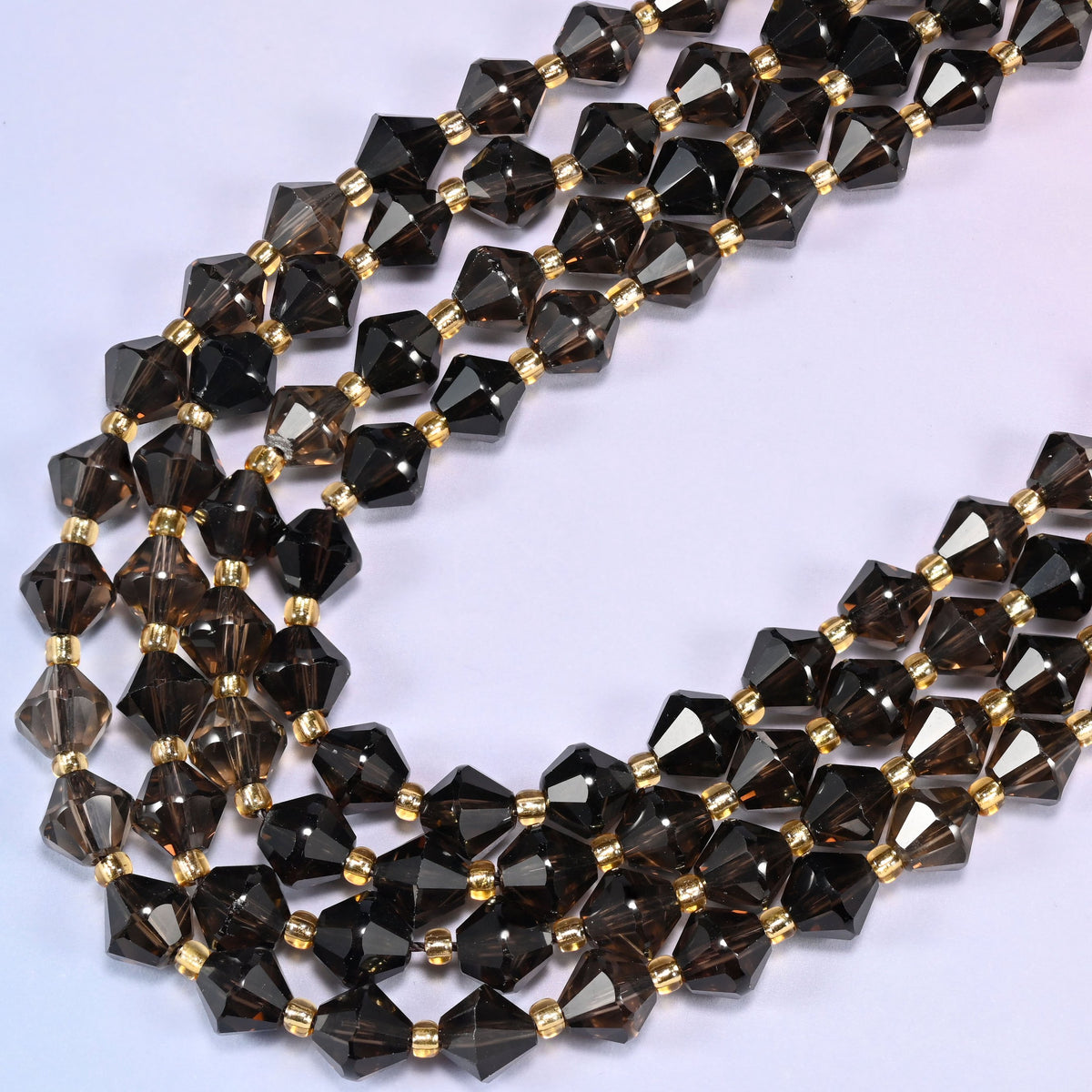 8mm Smoky Quartz faceted bicone beads arranged in a loose curved strand on a light lavender background.