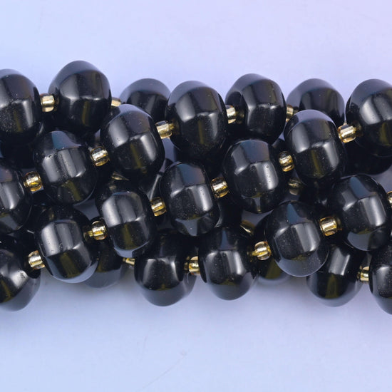 Close macro of black obsidian pumpkin beads, glassy surface reflecting a bright highlight