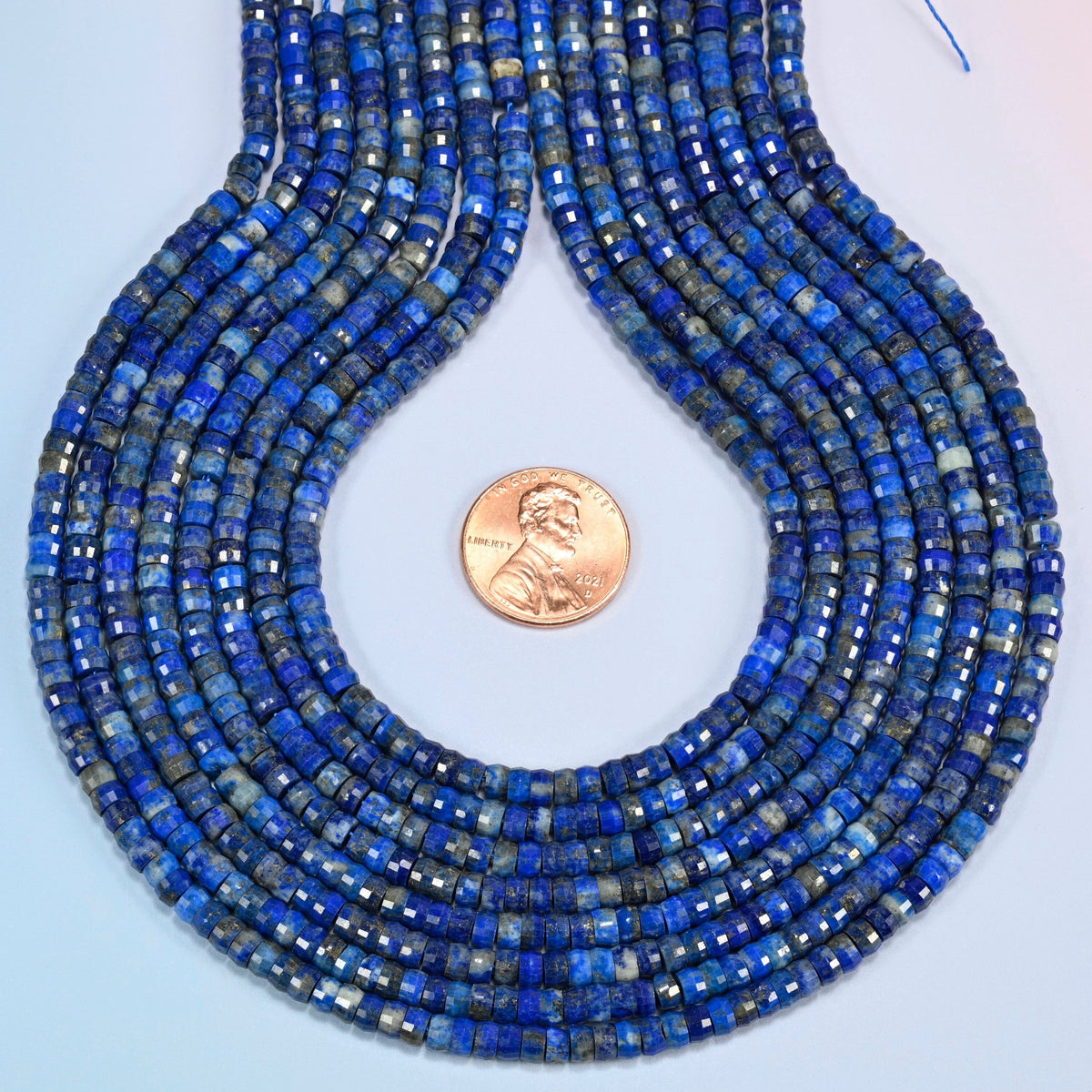 Lapis faceted heishi disc strands formed into a teardrop loop around a US penny for scale