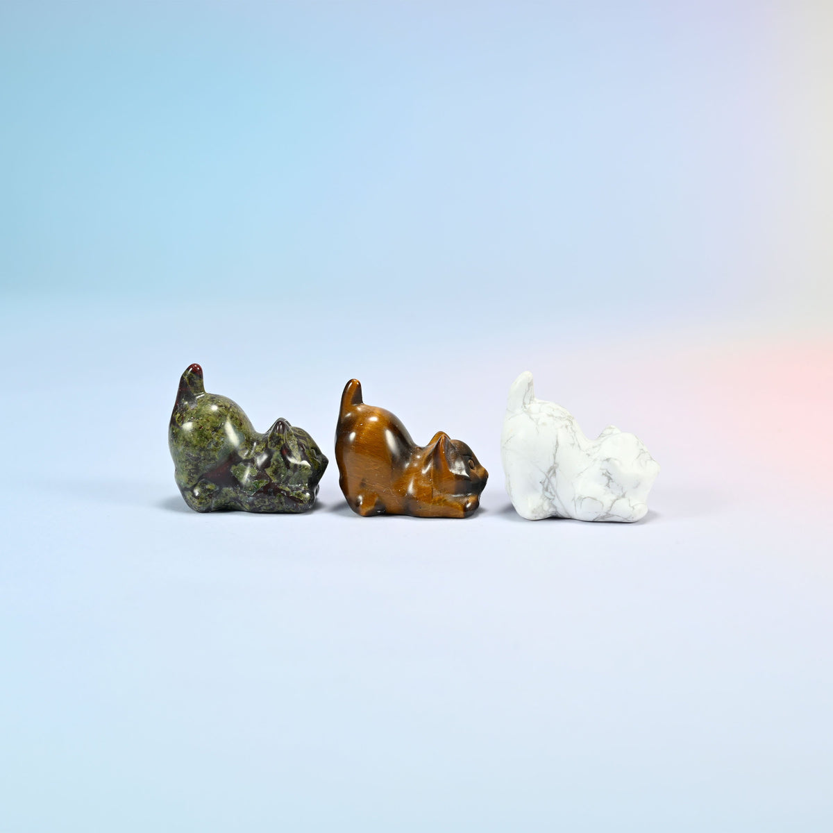 Side view of natural dragon bloodstone, tiger eye and white howlite yoga cat carvings crouched low with their tails curled up