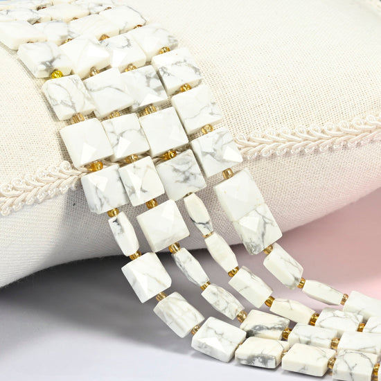 White howlite faceted flat square beads 10x10mm with small gold seed bead spacers, several strands draped over a white cushion