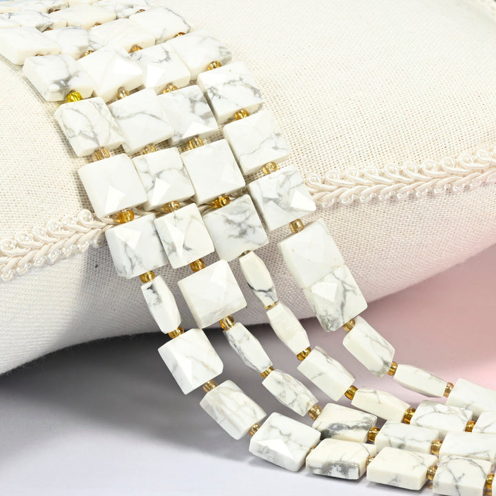 White howlite faceted flat square beads 10x10mm with small gold seed bead spacers, several strands draped over a white cushion