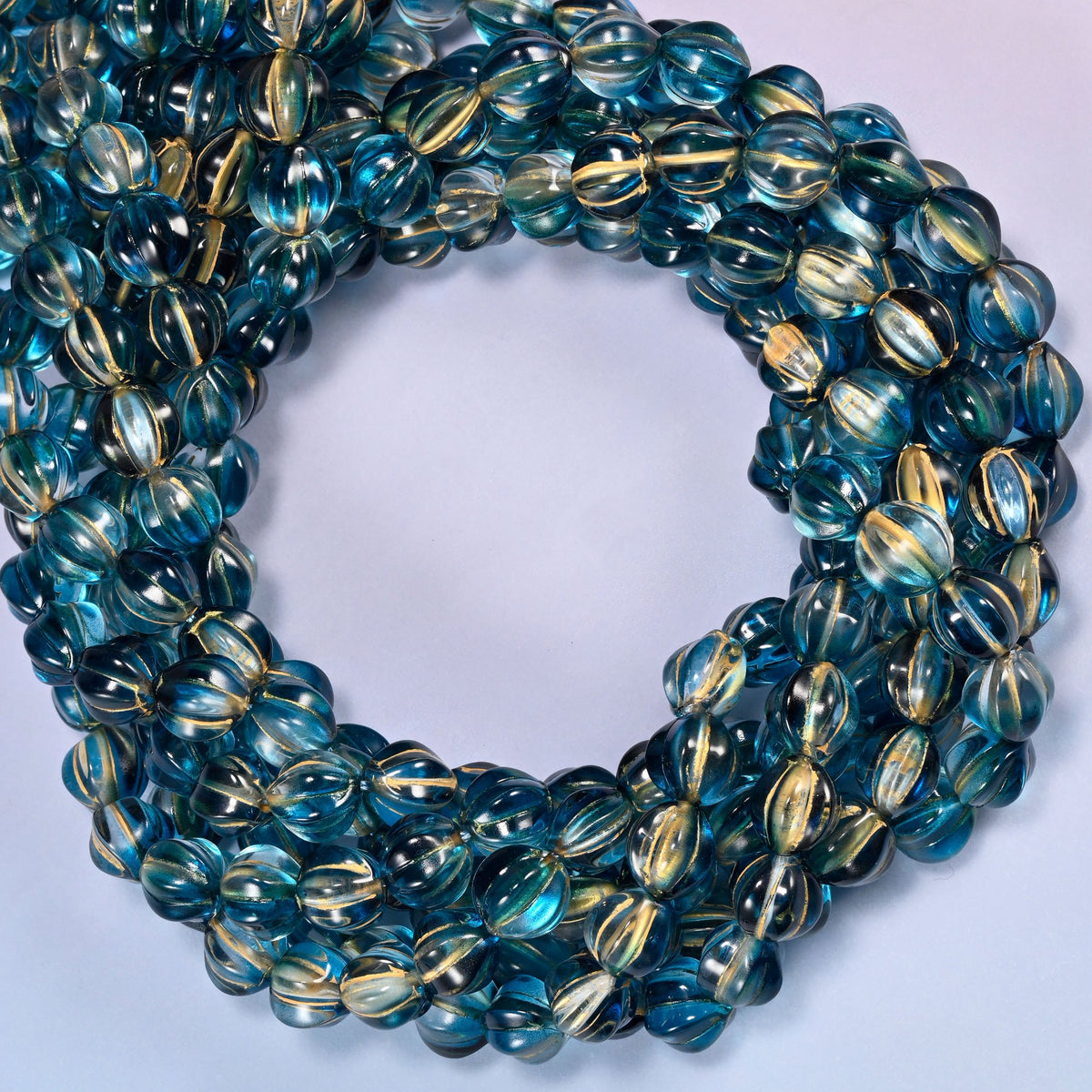 Dark blue gold pumpkin glass beads coiled with the open center to one side, showing the fluted grooves end on.