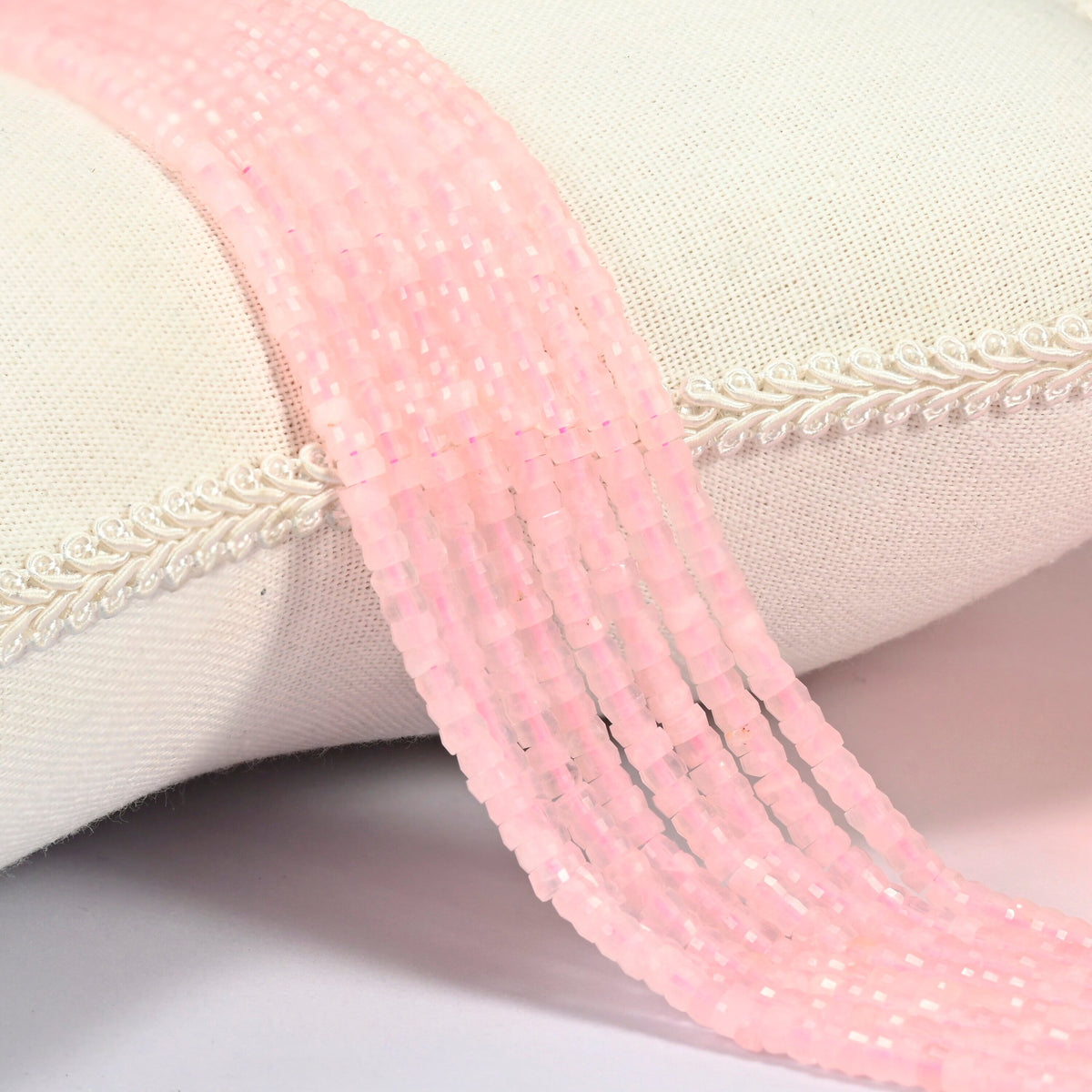 Rose quartz faceted heishi disc beads 2x4mm, several strands draped over a white cushion