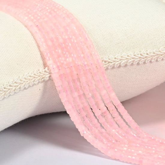 Rose quartz faceted heishi disc beads 2x4mm, several strands draped over a white cushion