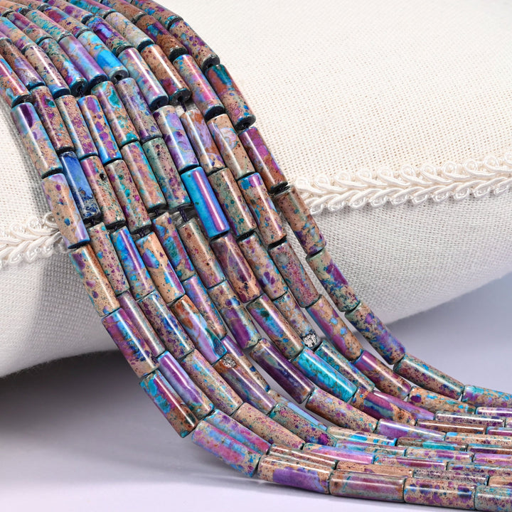Close-up of multiple strands of purple, magenta, and turquoise dyed Sea Sediment Jasper tube beads draped over a cream fabric jewelry display bust.
