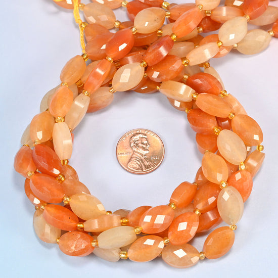 Red aventurine faceted flat oval beads 9x14mm coiled in a loop around a US penny for scale, close-up of the faceted flat oval shape