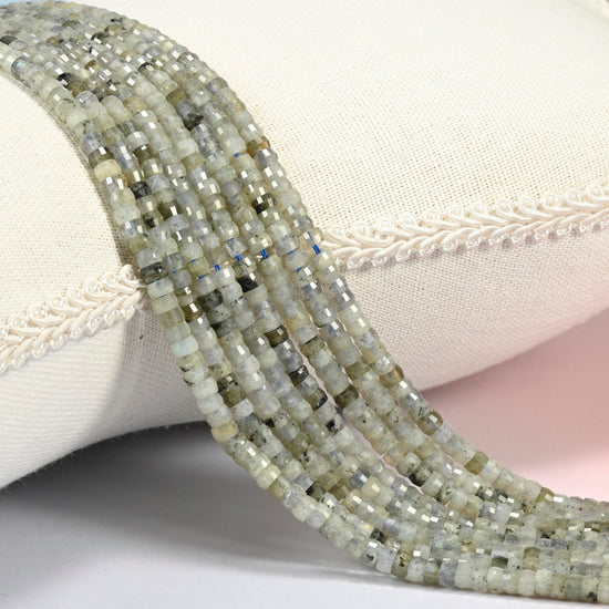 White labradorite faceted heishi disc beads 2x4mm, several strands draped over a white cushion