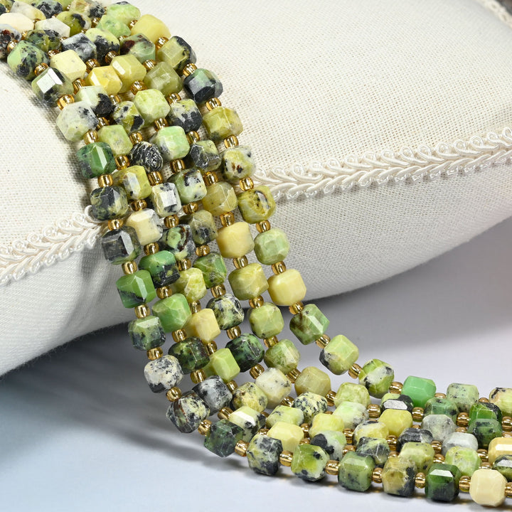 Yellow howlite faceted cube beads 6mm with small gold spacer beads, several strands draped over a white cushion
