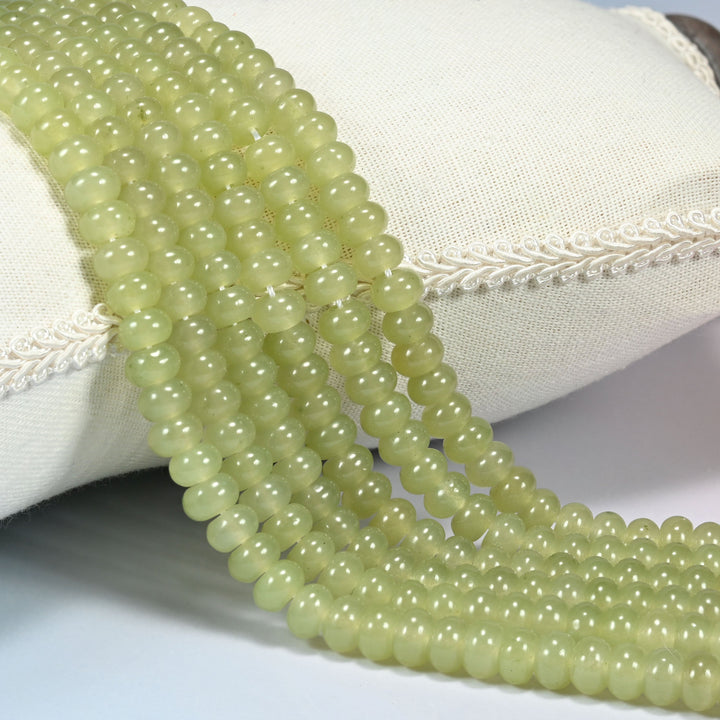 Green Grape dyed jade gemstone rondelle beads draped over a cushion in soft rows, a soft yellow green, the color of a green grape, even the length of the strand