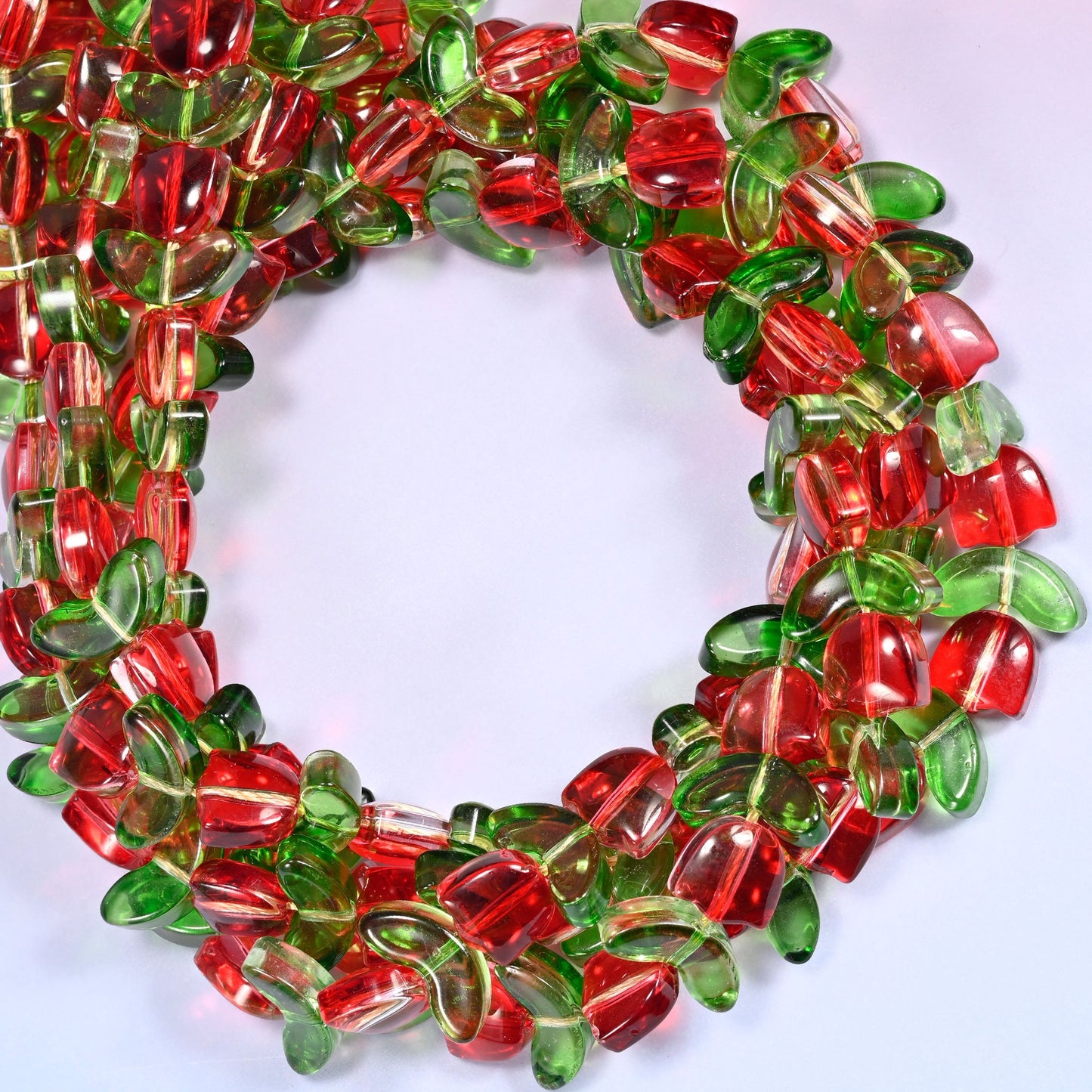 Horizontal row of red tulip and green leaf glass beads laid straight across a lavender and pink gradient background.