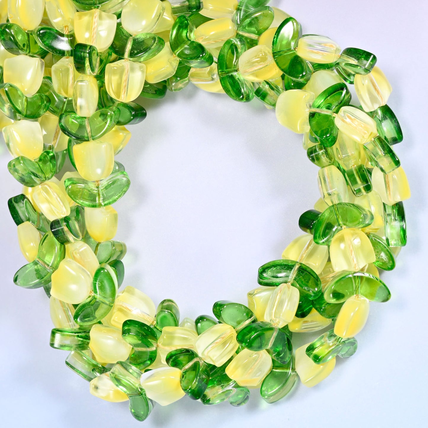 Horizontal row of yellow tulip and green leaf glass beads laid straight across a lavender and pink gradient background.