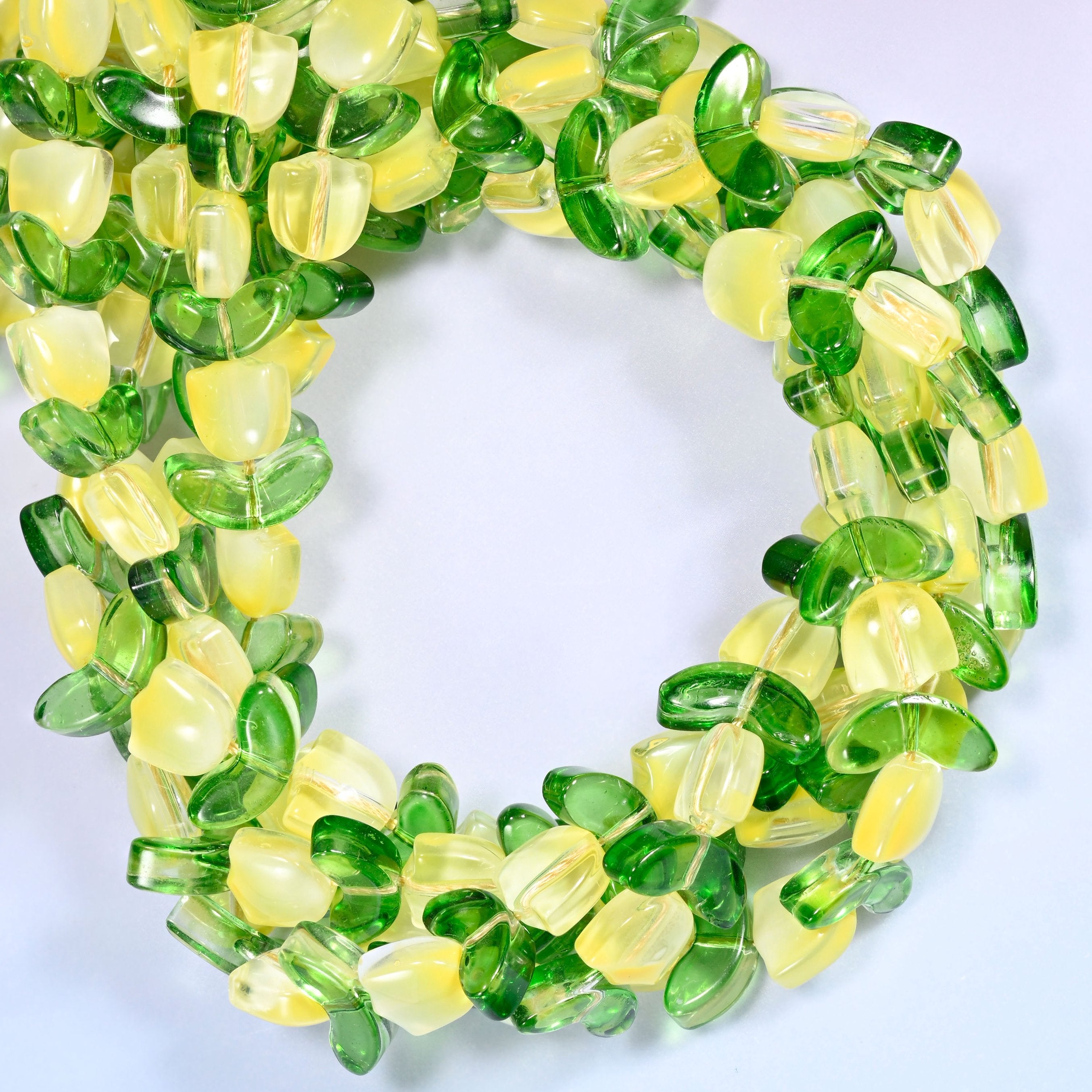 Horizontal row of yellow tulip and green leaf glass beads laid straight across a lavender and pink gradient background.