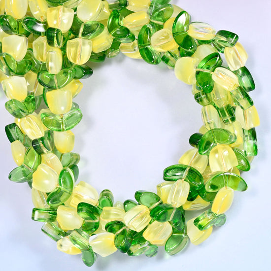Horizontal row of yellow tulip and green leaf glass beads laid straight across a lavender and pink gradient background.