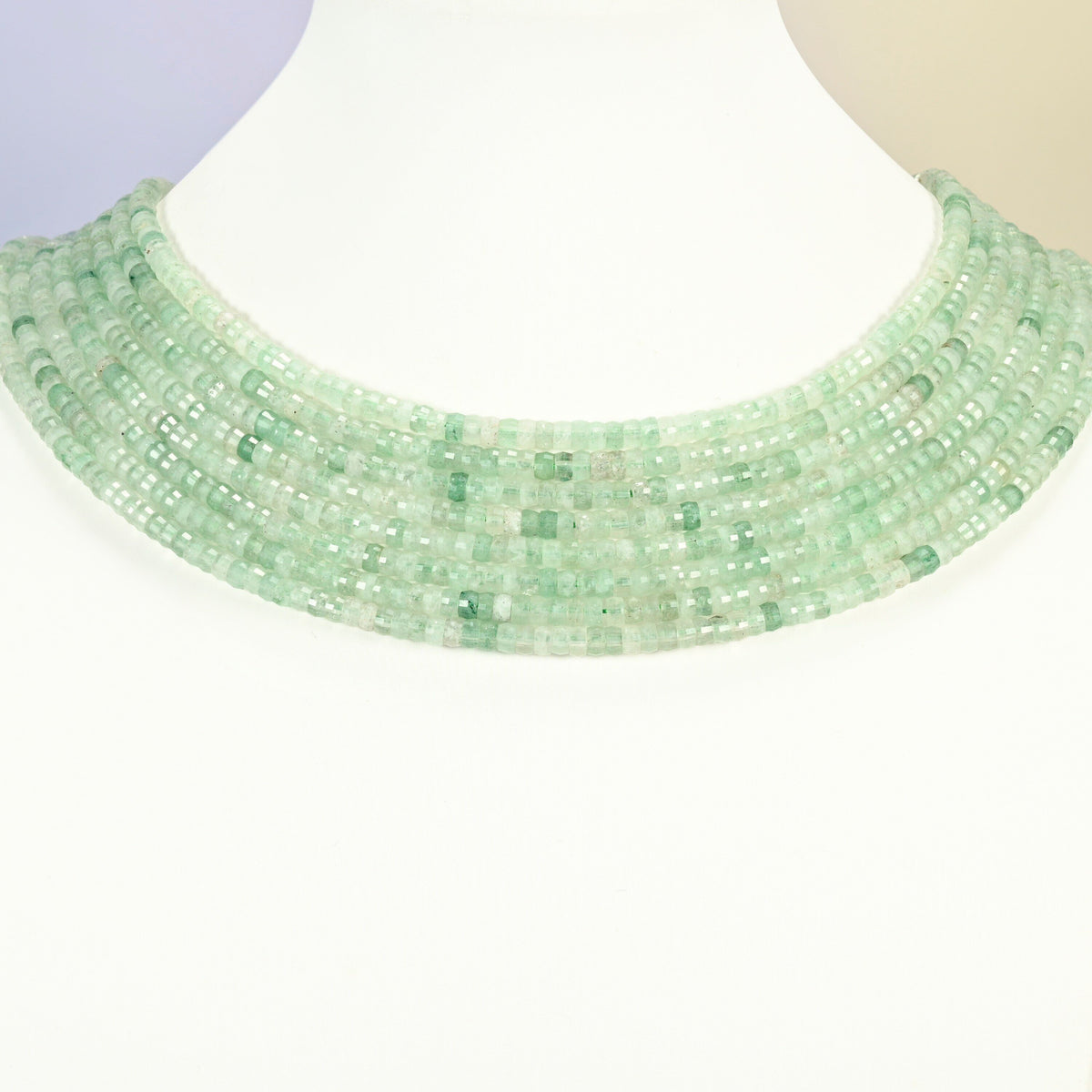 Green strawberry quartz faceted heishi disc strands arranged as a layered collar on a white display bust, light green beads across the neck