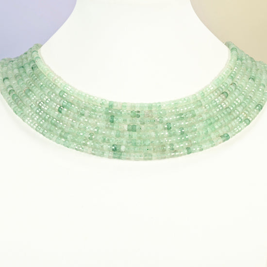 Green strawberry quartz faceted heishi disc strands arranged as a layered collar on a white display bust, light green beads across the neck